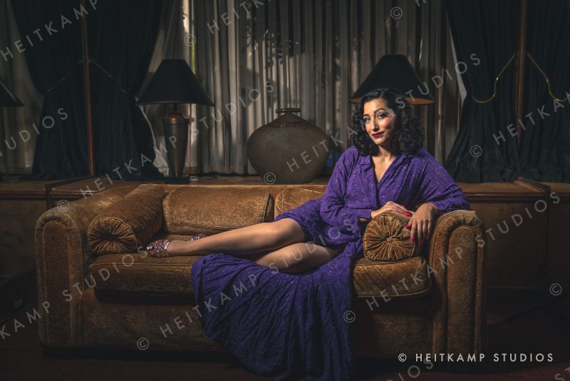 Artemisa lounging on a vintage velvet sofa in a flowing purple robe