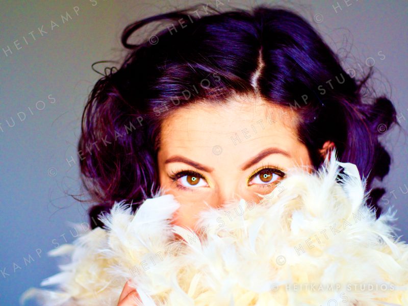 Artemisa peeking over a cream feather boa, only her eyes showing